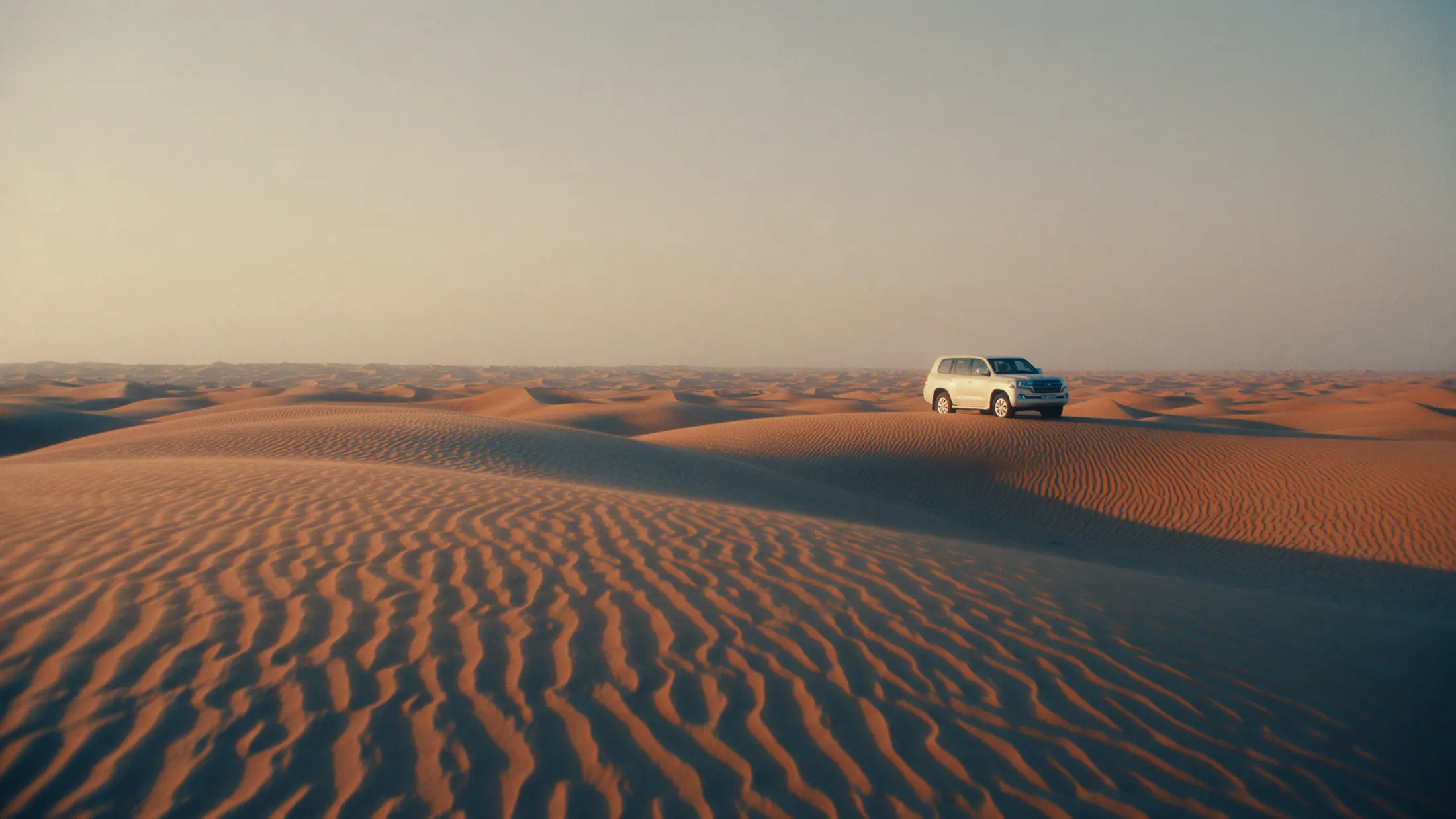 Rippled orange dunes of the Wahiba Sands with a white 4x4 on a crest